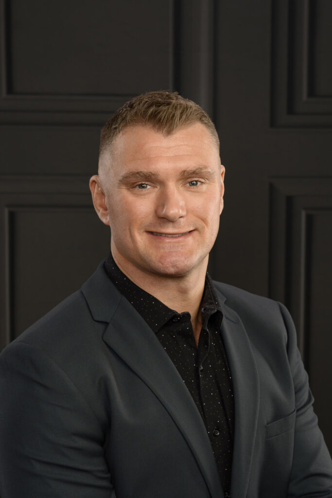 studio headshot of a man on a dark wainscotting background