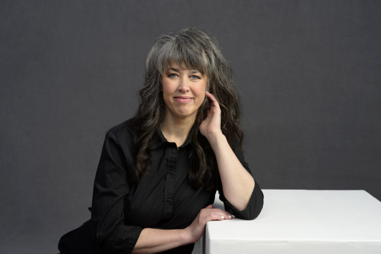 casual business headshot of woman leaning on a white box